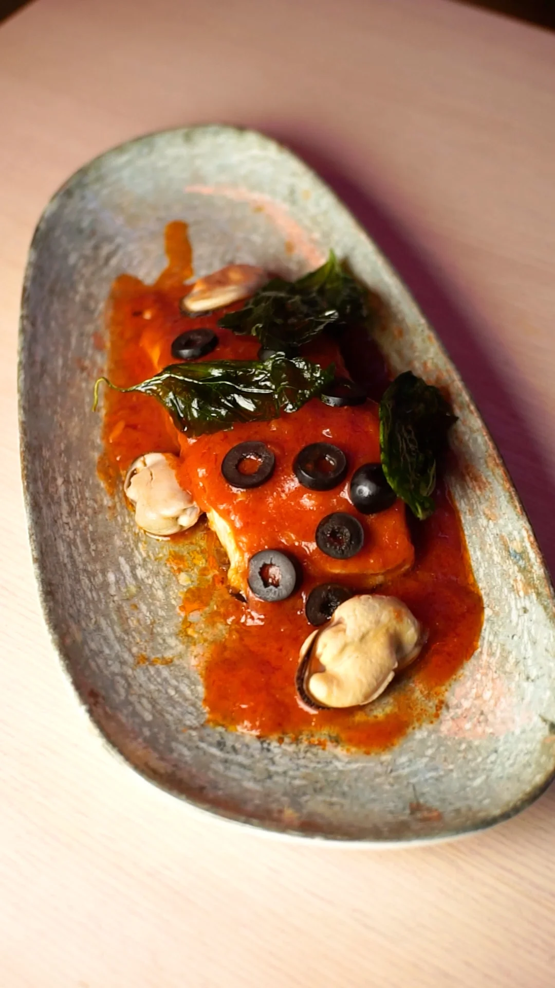 Baked sea bass in classic tomato and fresh basil sauce with black olives and a bed of mussels